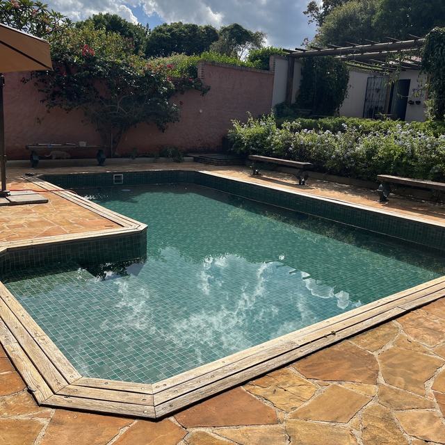 Piscina verde em jardim com piso de pedra e bancos