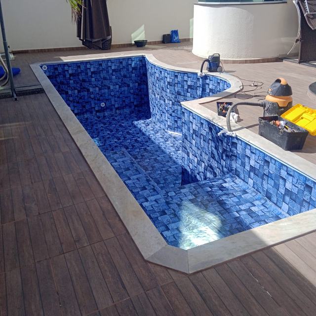Piscina de formato curvo com vinil azul, ainda vazia, em fase de acabamento