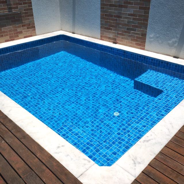 Piscina azul com banco interno, borda de mármore e deck de madeira